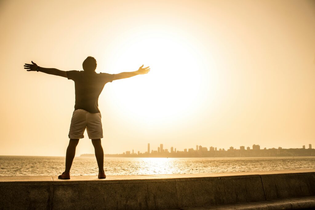 Man stands with arms outstretched facing the sunset over the ocean, capturing a moment of freedom and tranquility.